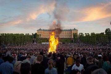 Et stort Sankt Hans bål med massevis af mennesker rundt omkring foran Frederiksberg Slot, som står flot under den farvede aftenhimmel